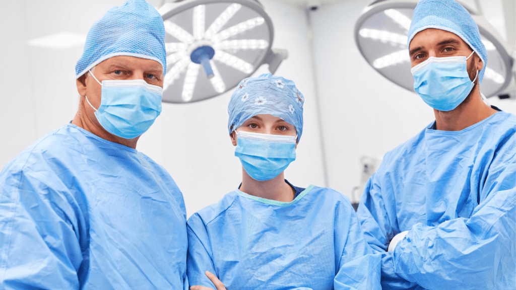 Three surgeons in blue scrubs stand in an operating room, focused and ready for a surgical procedure.