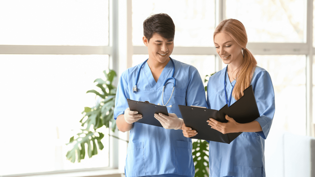 Two physician assistants stand side by side in front of a window, embodying care and collaboration in a medical environment.