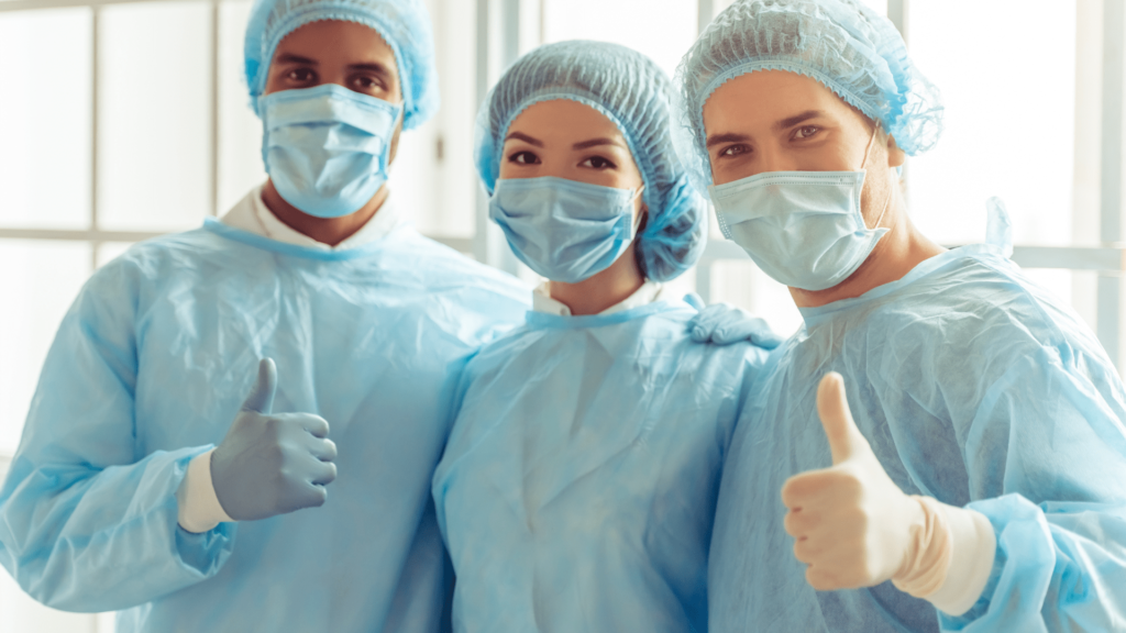 Three healthcare professionals in scrubs enthusiastically giving thumbs up, symbolizing support and camaraderie in their work.