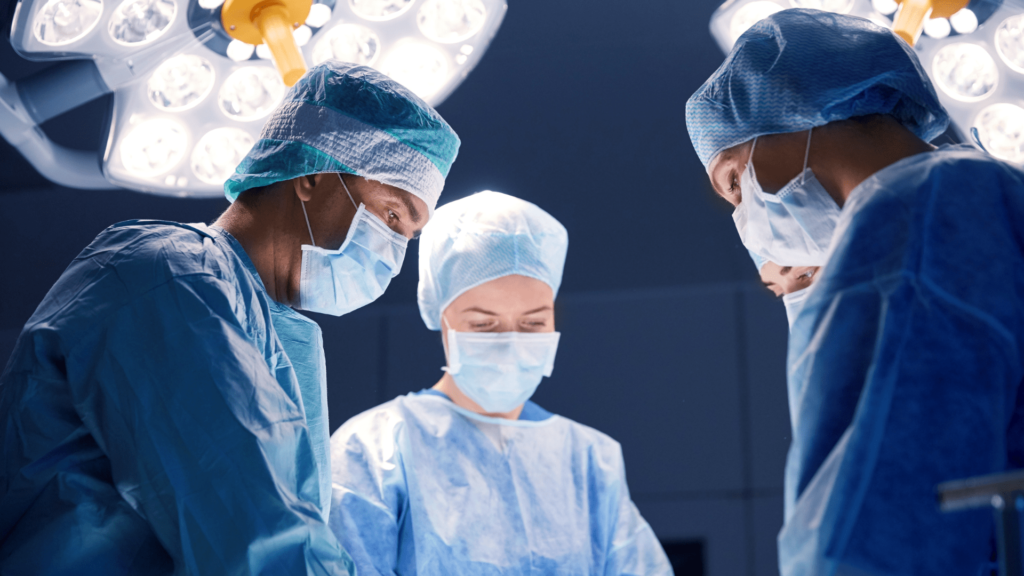 Three surgeons in blue scrubs and surgical masks collaborate in a sterile operating room environment.